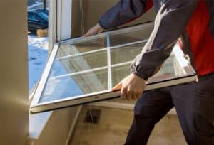 Window installation with a worker handling a white-framed window panel inside a home.