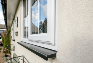 Close-up of a white-framed exterior window with a dark sill on a stucco house, reflecting blue sky and nearby homes.